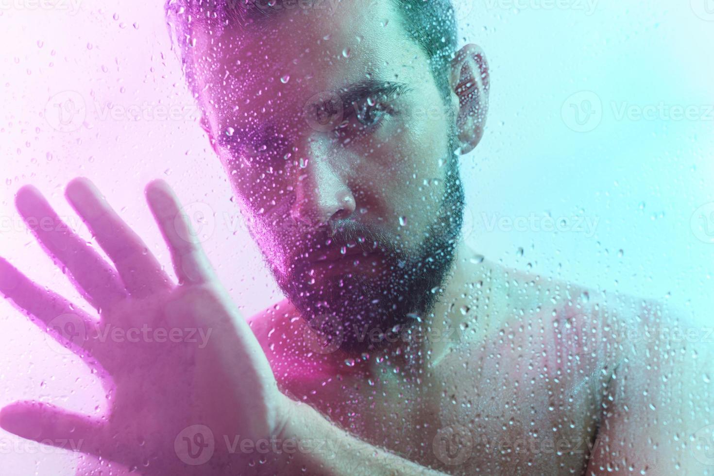 Portrait of handsome man through wet glass in neon light photo