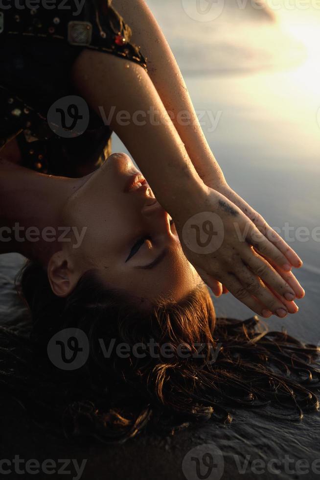 Sexy woman wearing black tunic is posing on the beach with black sand photo