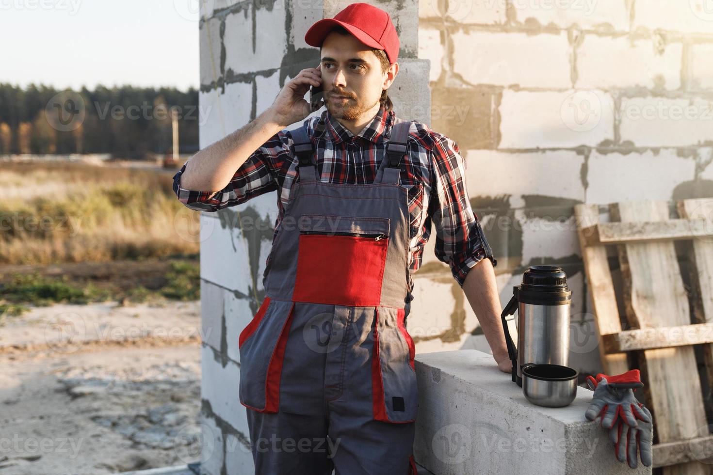 albañil hablando por teléfono inteligente en el sitio de construcción foto