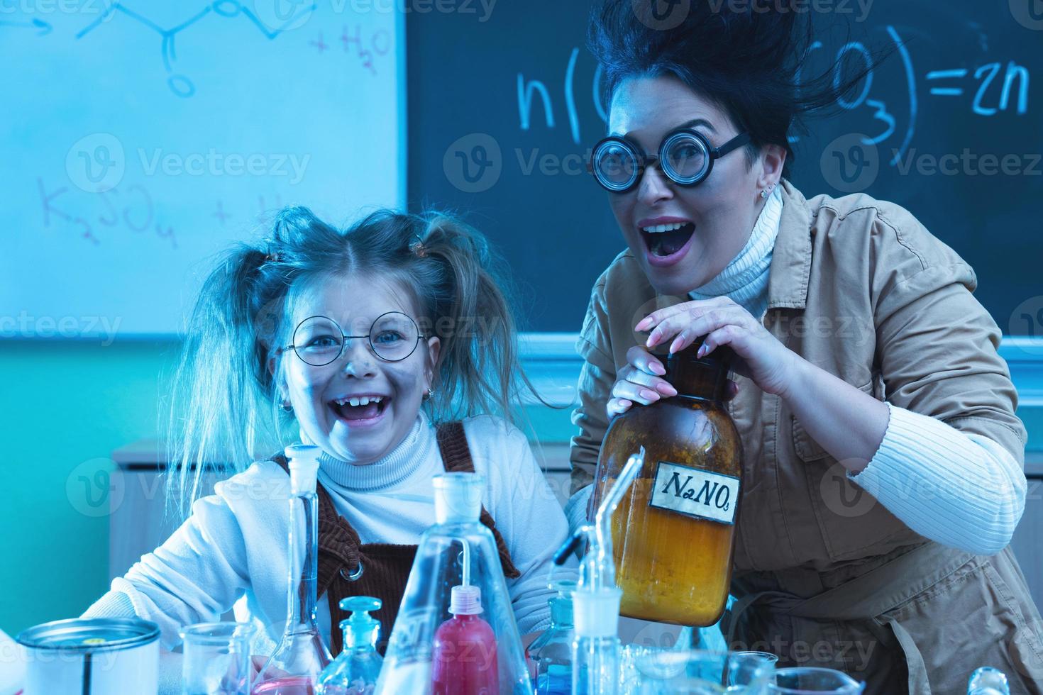 Teacher and little girl during chemistry lesson mixing chemicals in a laboratory photo