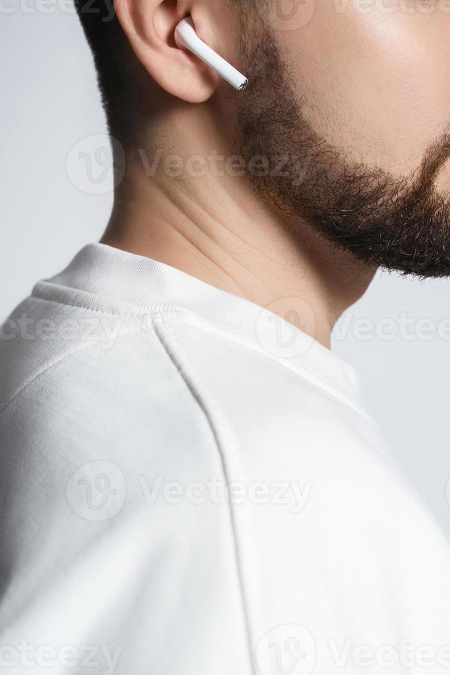 Bearded man in white clothes using wireless earbuds photo