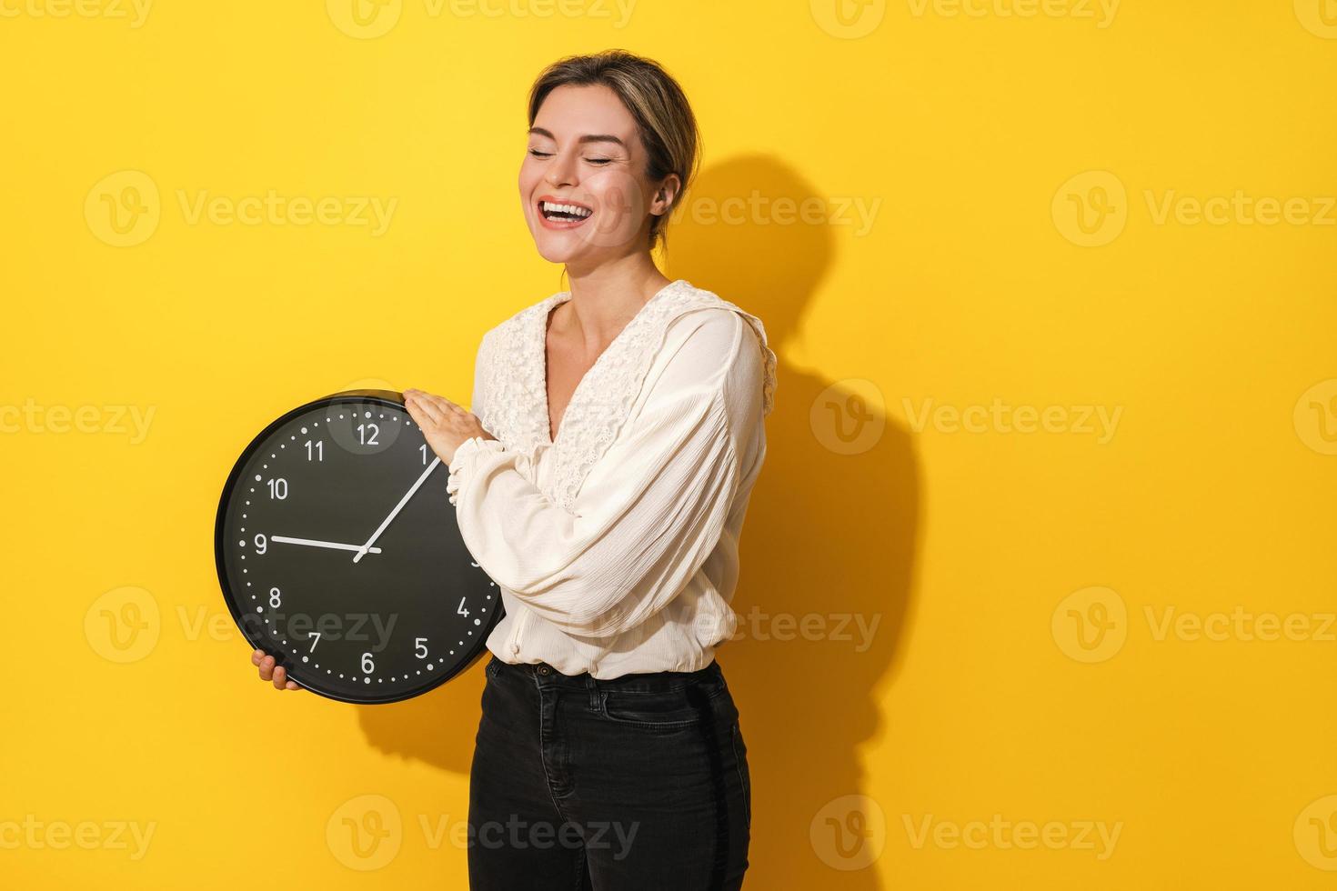 Cheerful woman holding big clock on yellow background photo
