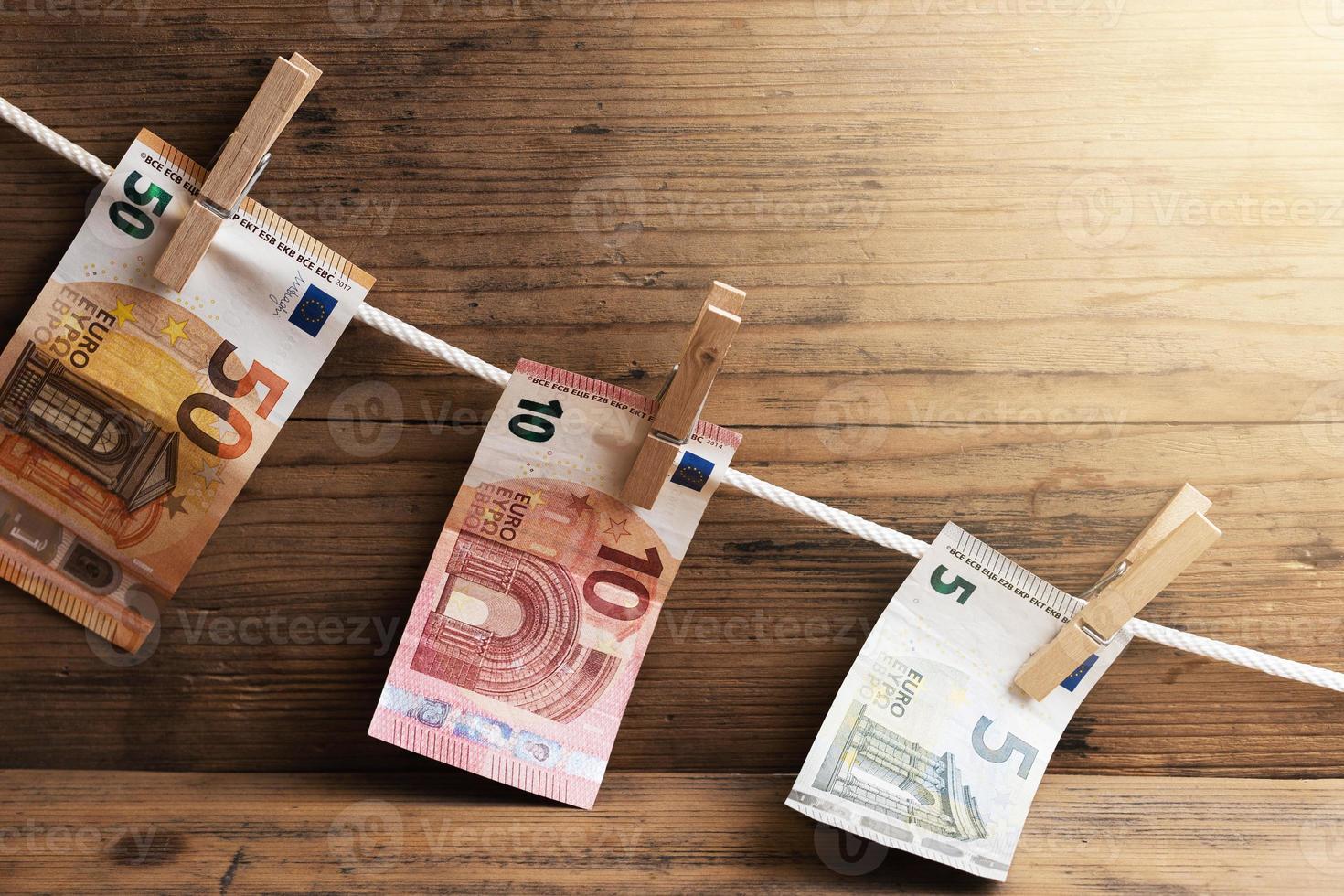 Euro banknotes of different value are drying on a white rope, held by clothespins. photo