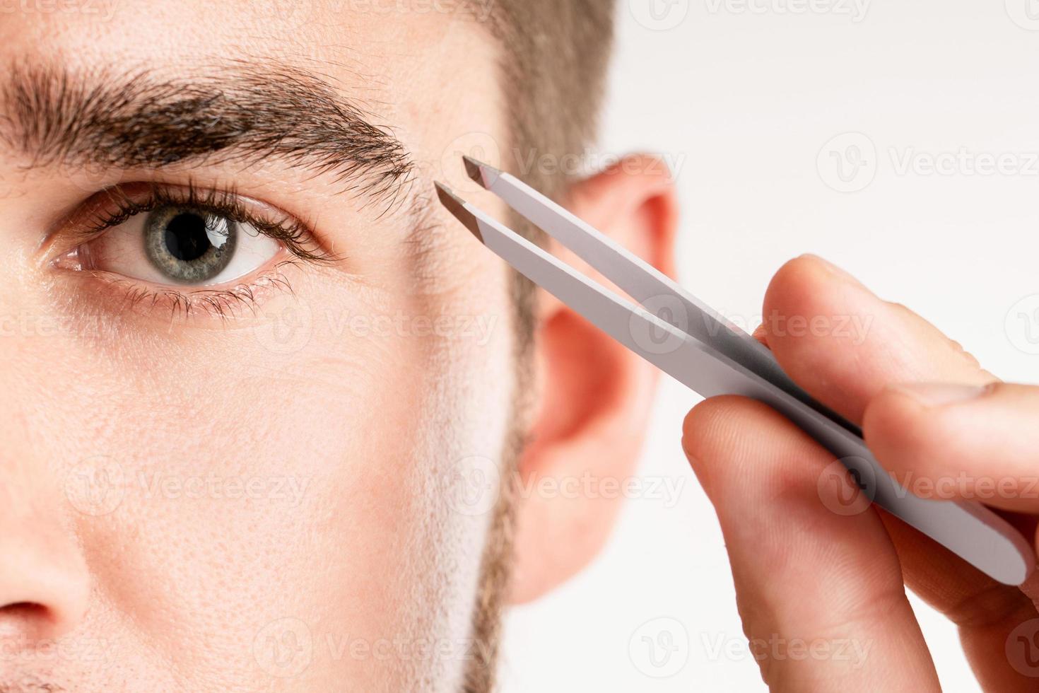 Male eye and tweezers for eyebrow grooming and shape correction photo