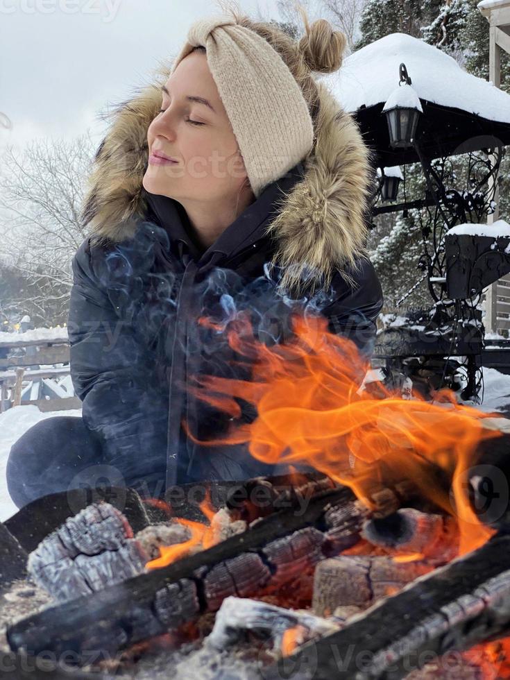 mujer joven calentándose junto a la fogata durante el frío día de invierno foto