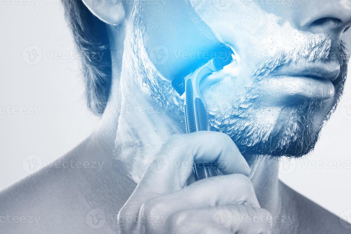 Young man using sharp safety razor for a shaving routine photo