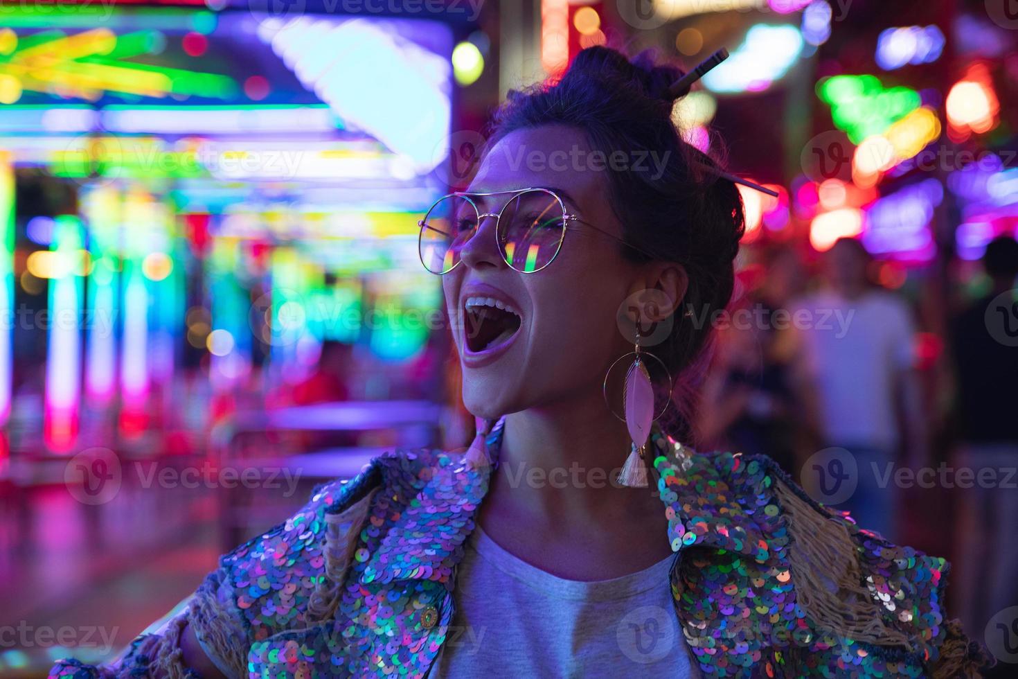 mujer elegante con chaqueta con lentejuelas brillantes en la calle de la ciudad con luces de neón foto