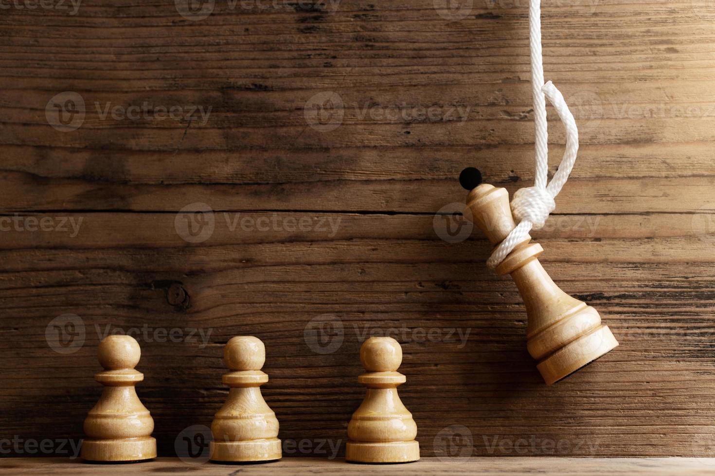 Wooden chess queen hanging on a white rope with pawns standing below. photo