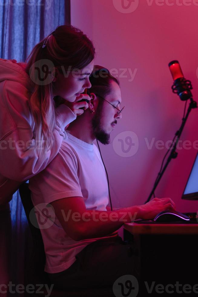 Young couple in room with neon light are using modern personal computer photo