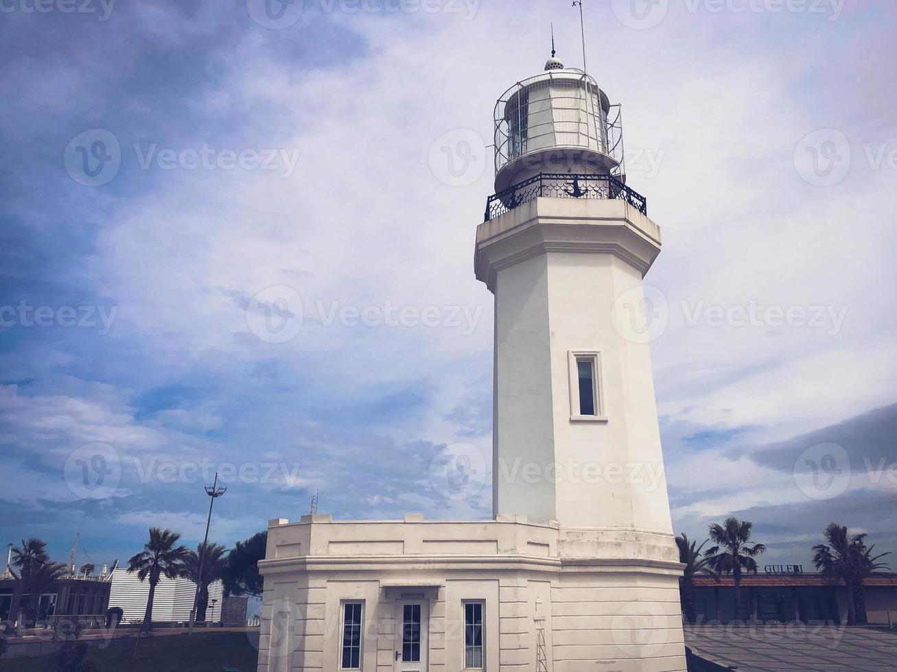 Big tall stone white lighthouse on the tropical sea warm summer resort with palm trees against the blue sky photo