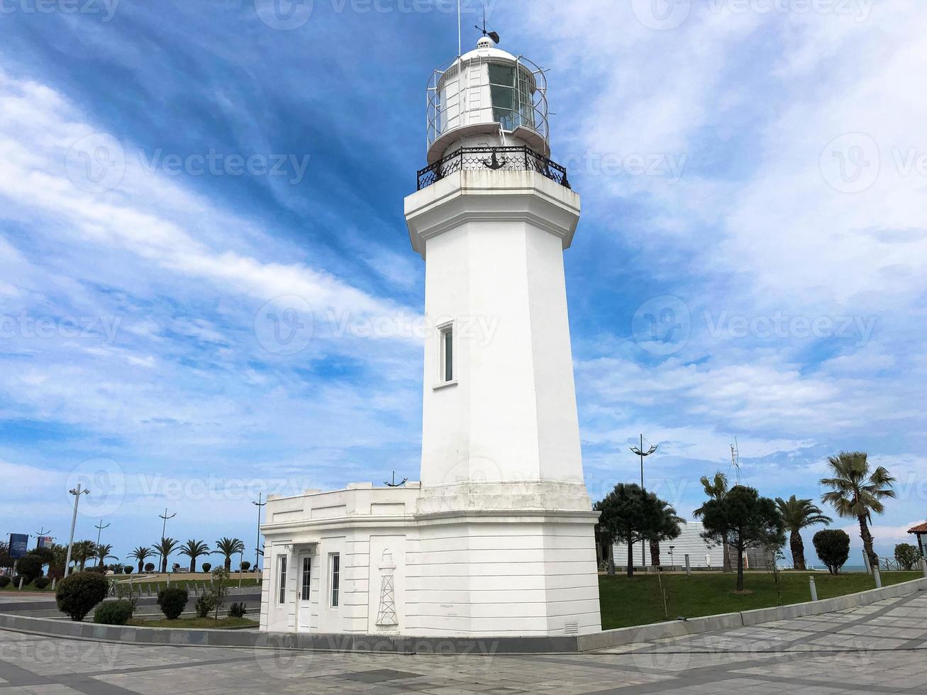 Big tall stone white lighthouse on the tropical sea warm summer resort with palm trees against the blue sky photo