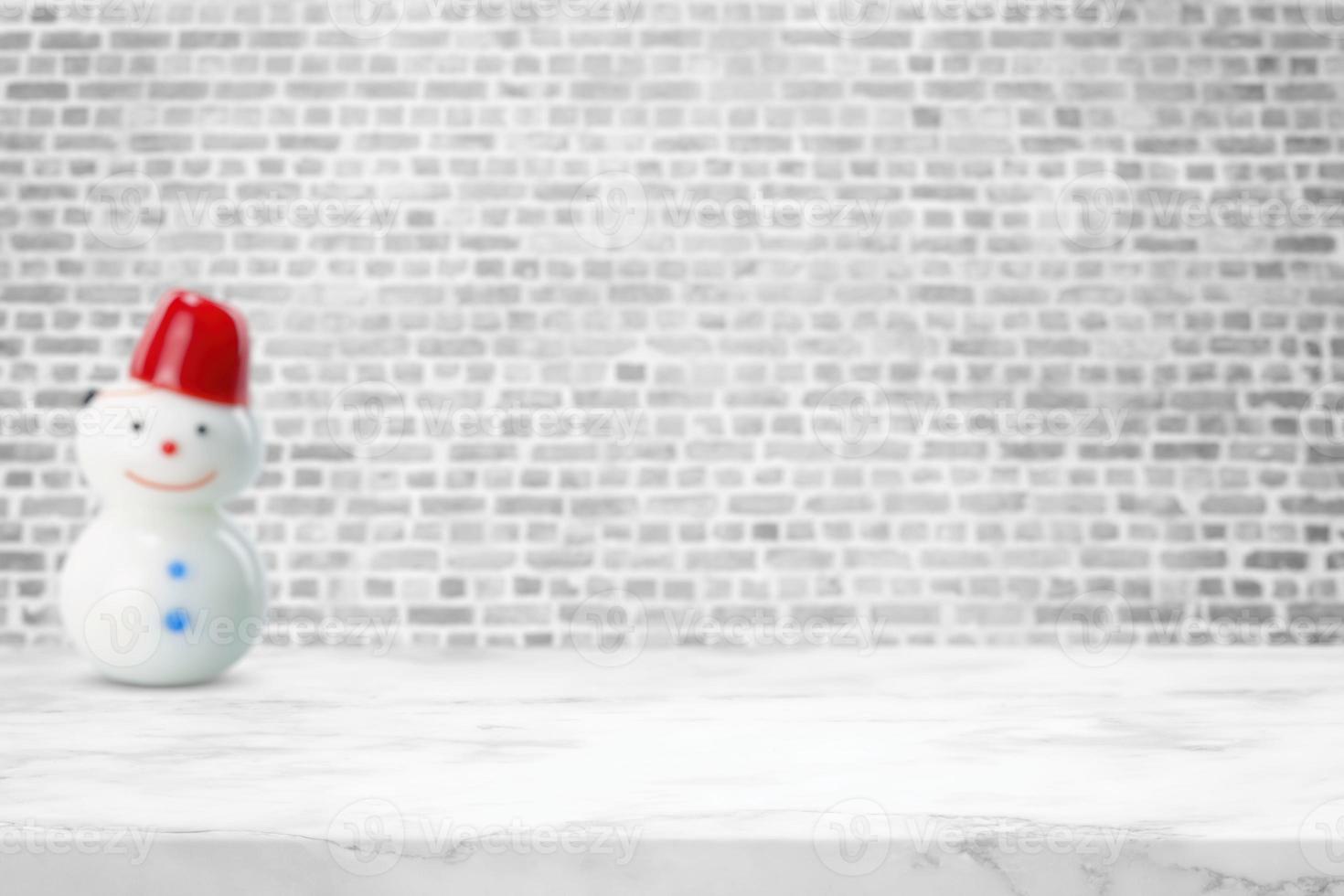 mesa de mármol blanco con enfoque selectivo en la superficie con fondo de pared de ladrillo borroso con muñeca de muñeco de nieve, adecuada para el telón de fondo de presentación del producto, exhibición y maqueta en el concepto de Navidad. foto