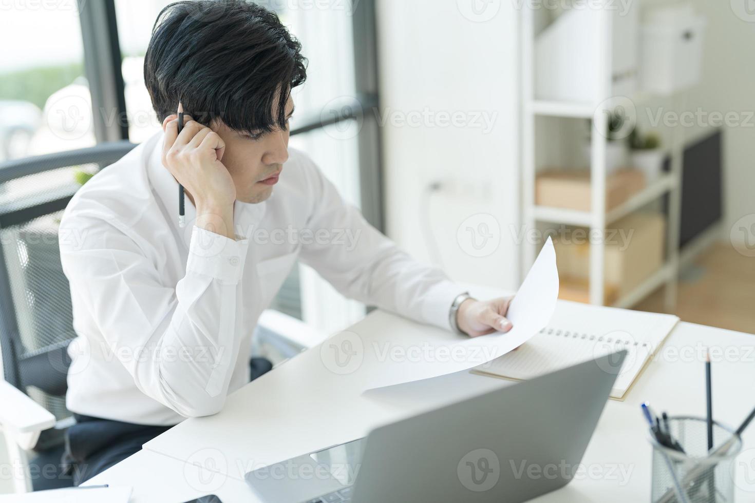 joven hombre de negocios sentado en su escritorio mirando Internet en su computadora portátil sintiéndose estresado. foto