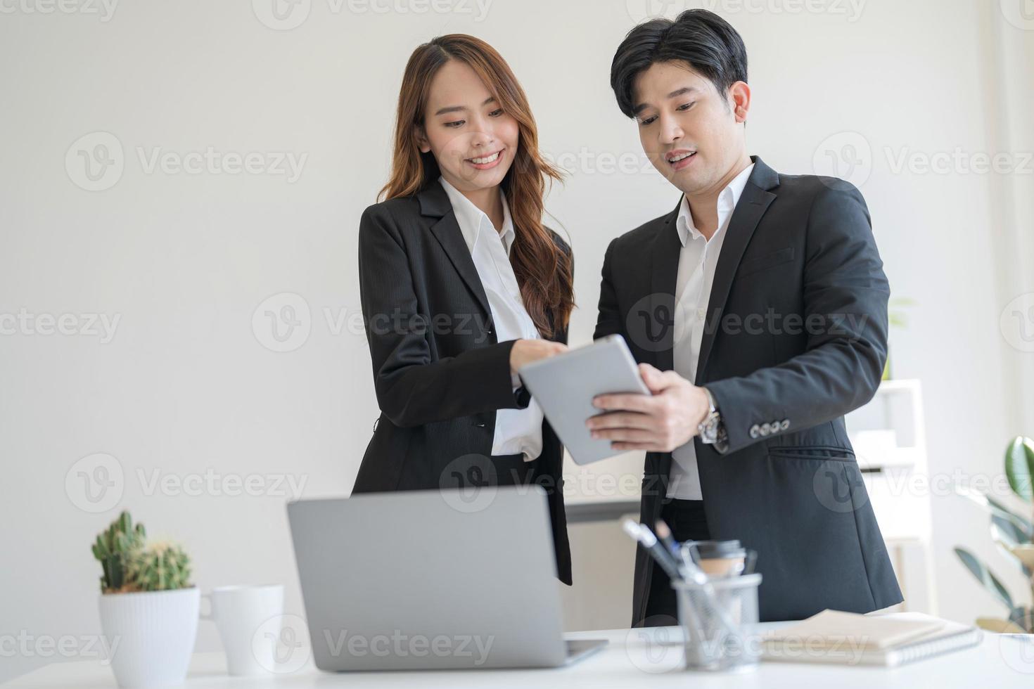 Business people stand together at a desk talking on their laptops photo