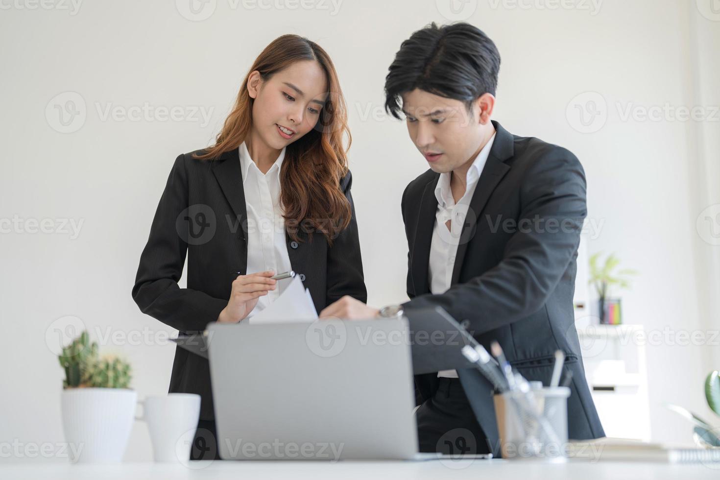 Business people stand together at a desk talking on their laptops photo
