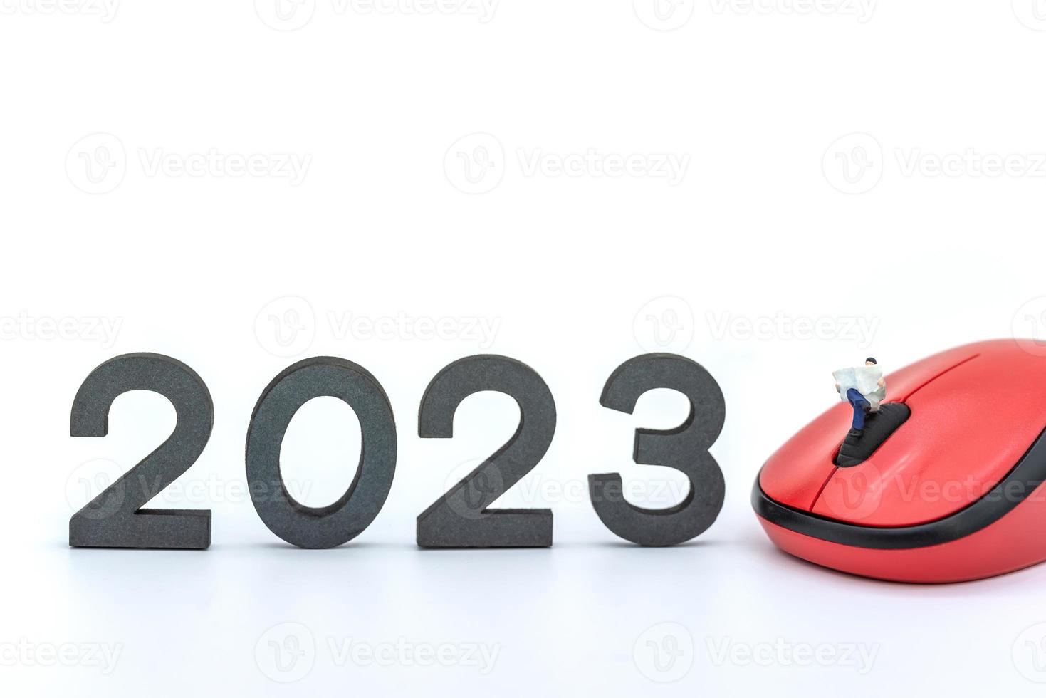 Concepto de año nuevo empresarial 2023. primer plano de figuras en miniatura de empresario sentado y leyendo un periódico en el ratón de la computadora con número sobre fondo blanco. foto