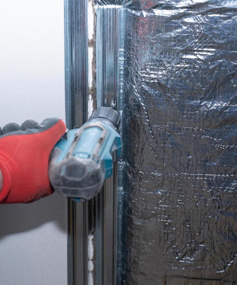 The master screws a metal profile to the wall with a screwdriver, warming the wall near the fireplace with mineral wool and foil. photo