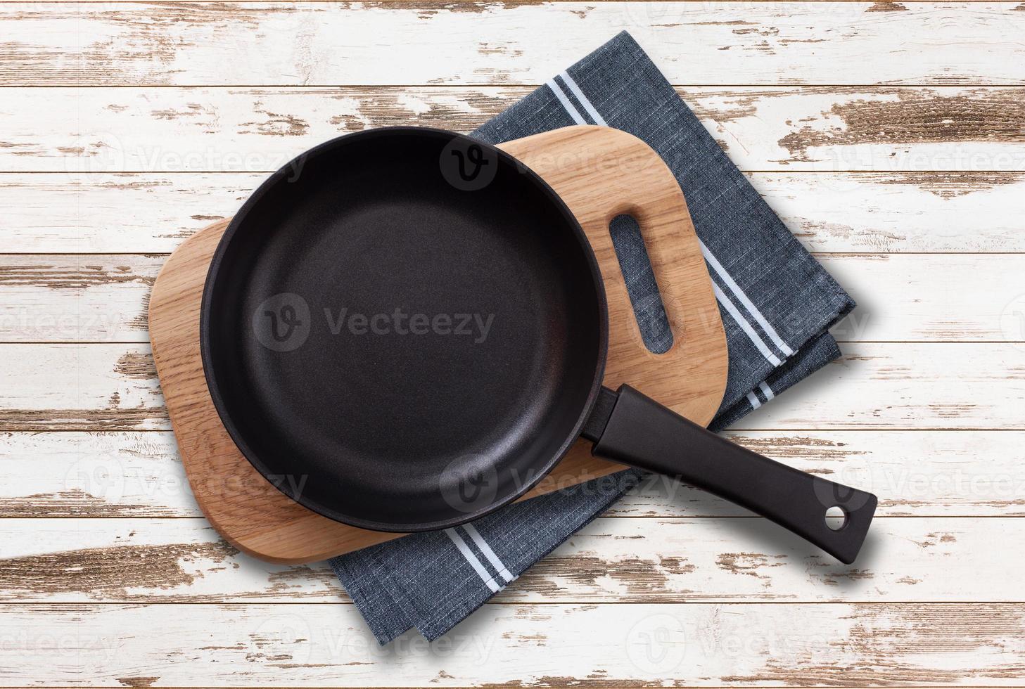 Black fry pan and board with napkin on wooden table. Top view mockup photo