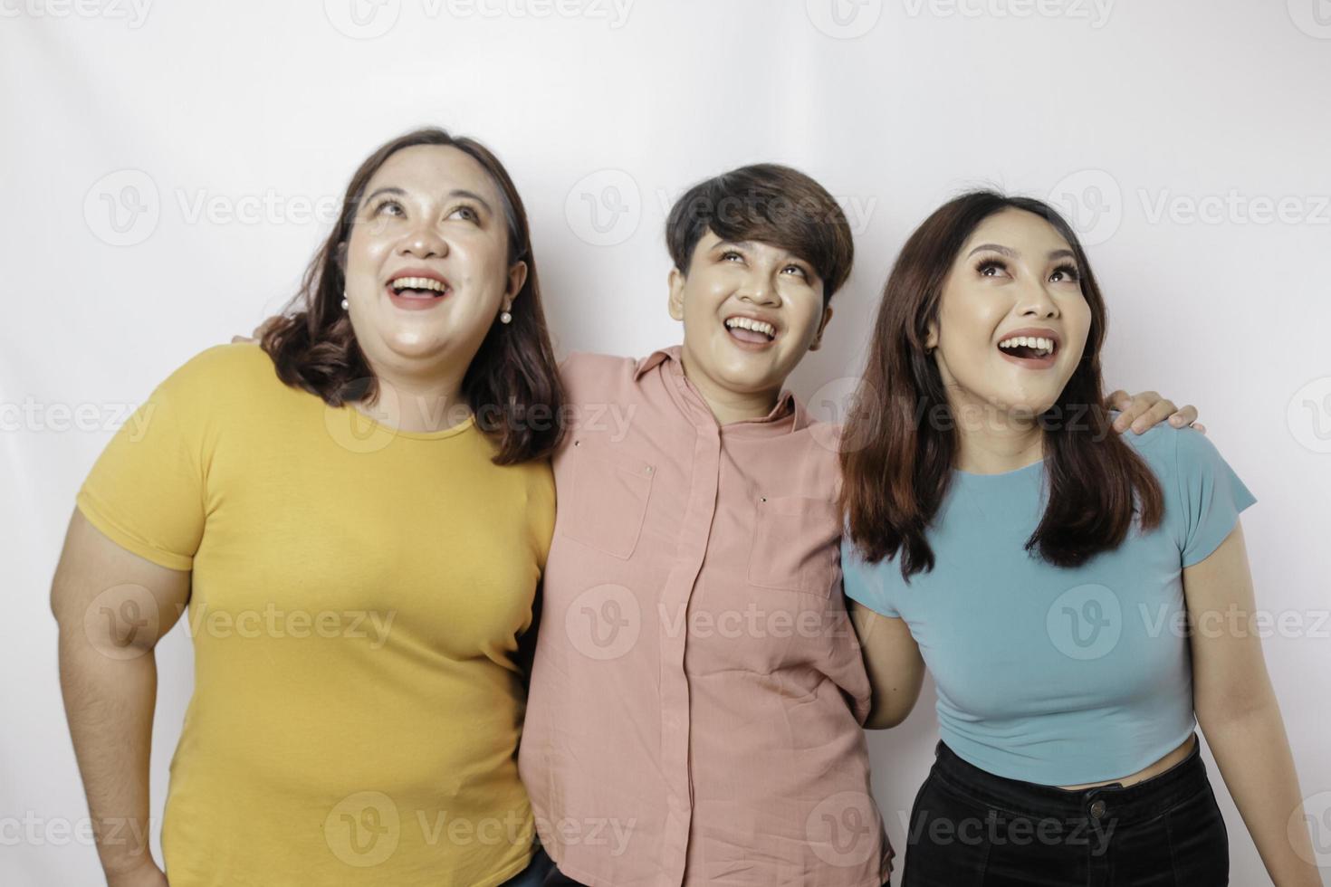 A portrait of three friends looks excited pointing at the copy space upside them, isolated by white background photo