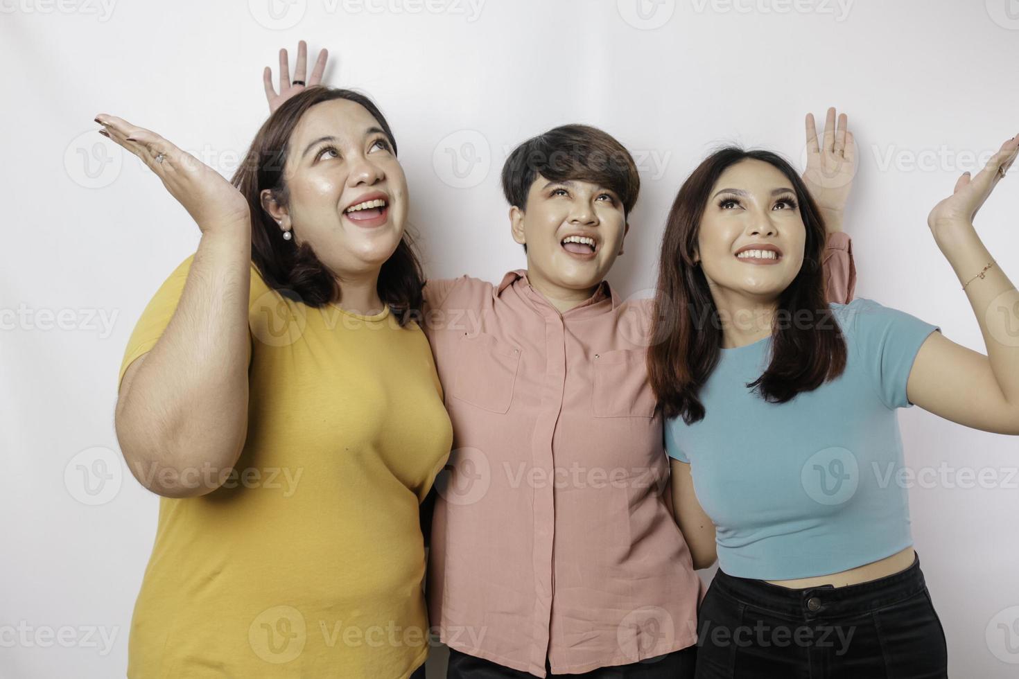 A portrait of three friends looks excited pointing at the copy space upside them, isolated by white background photo