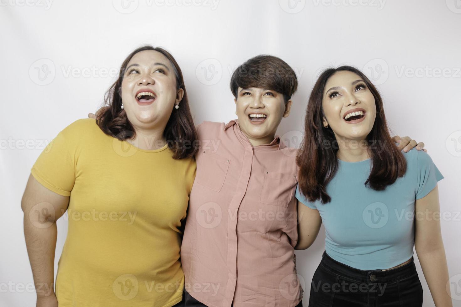 A portrait of three friends looks excited pointing at the copy space upside them, isolated by white background photo