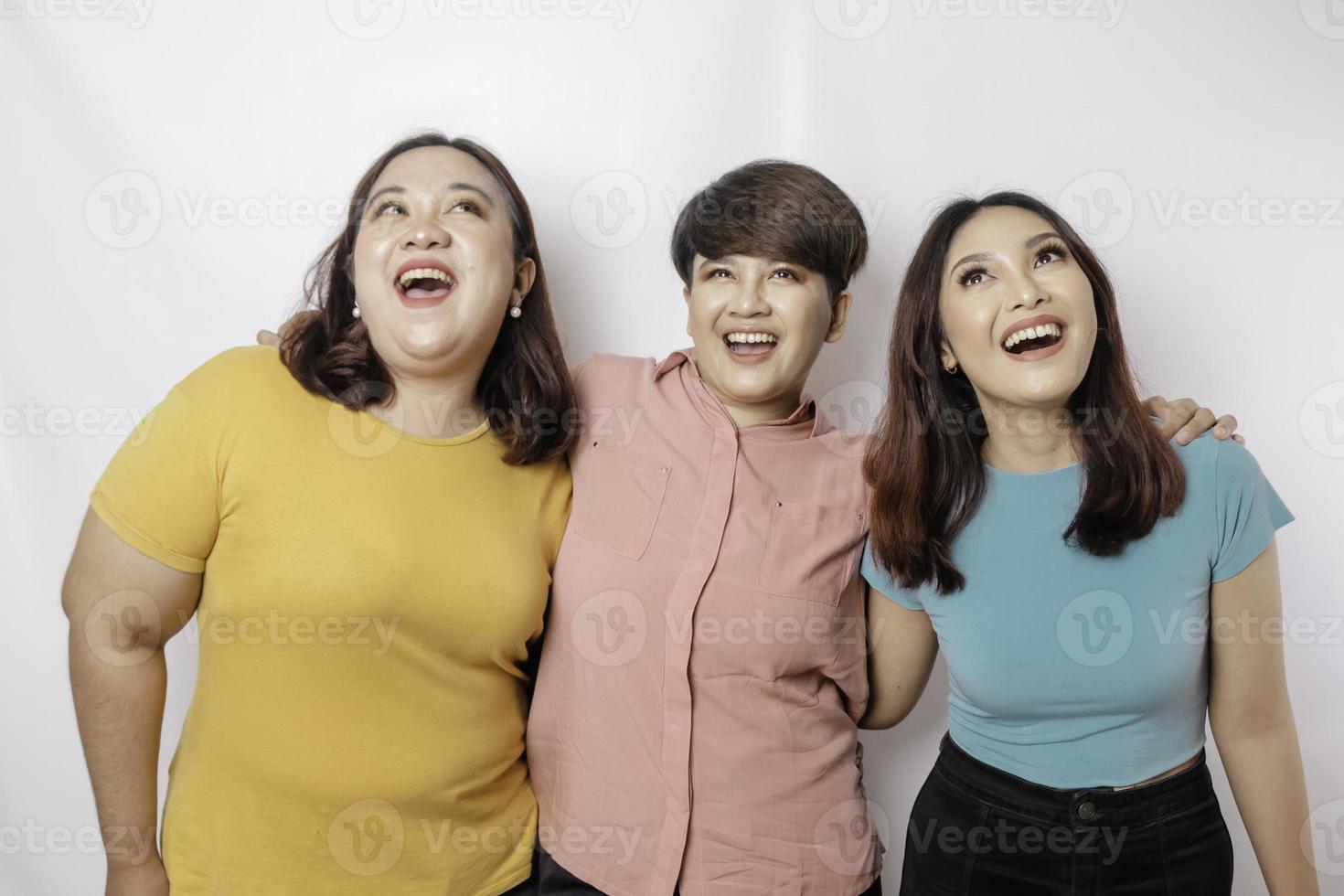 un retrato de tres amigos se ve emocionado señalando el espacio de copia al revés, aislado por fondo blanco foto