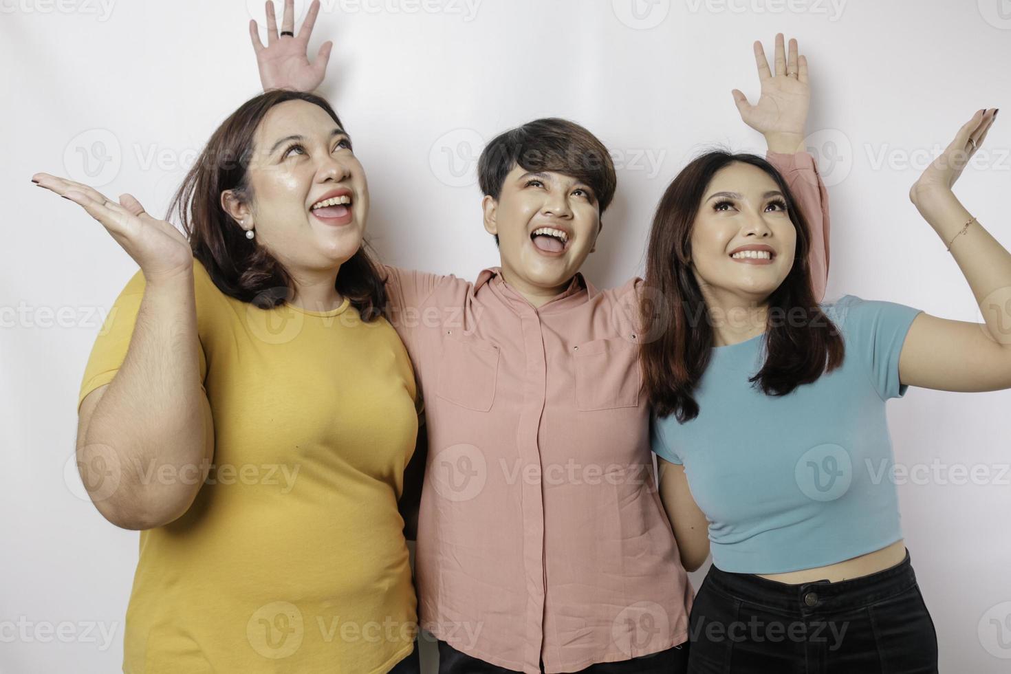 A portrait of three friends looks excited pointing at the copy space upside them, isolated by white background photo