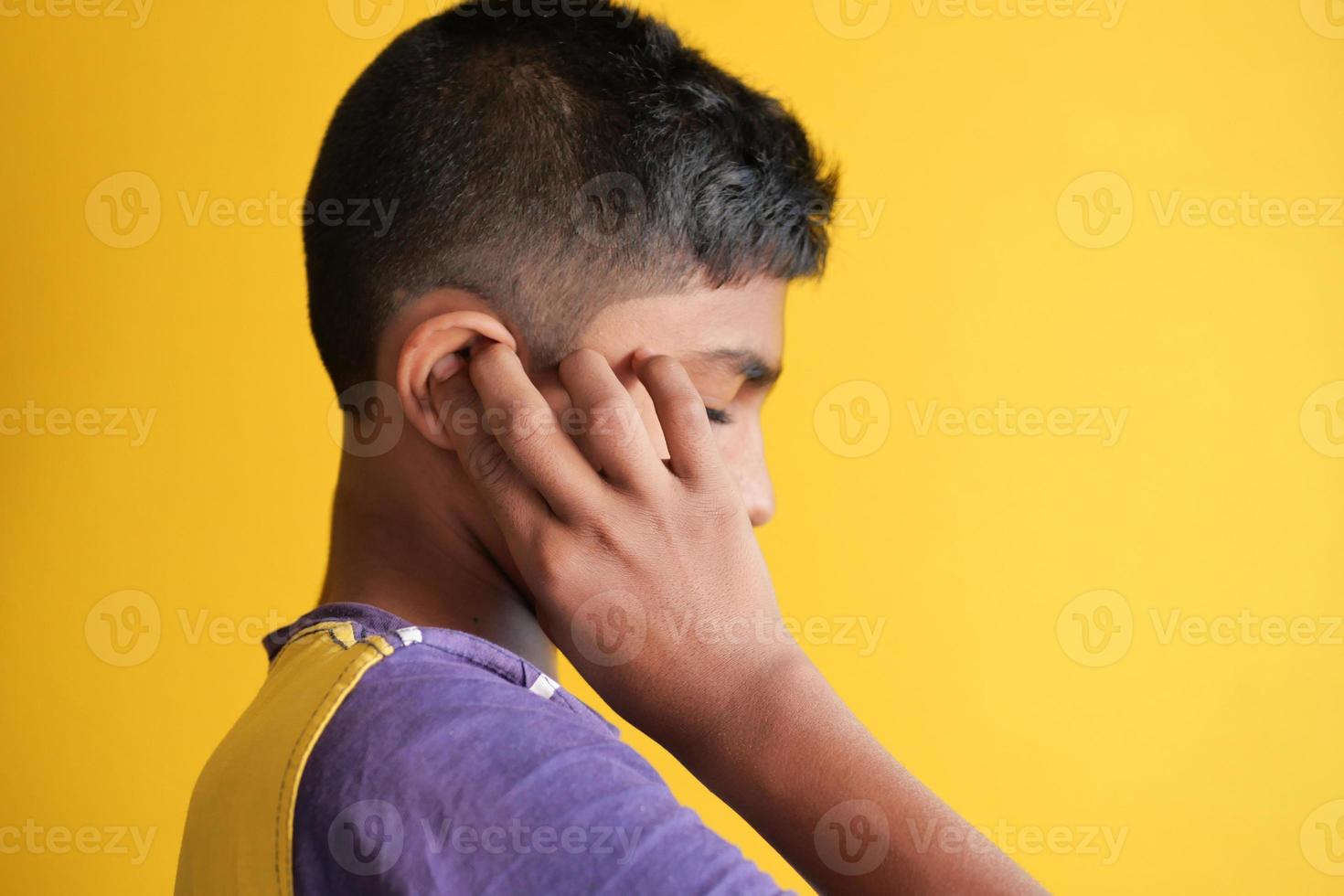 niño que tiene dolor de oído tocando su oído doloroso contra el fondo amarillo foto
