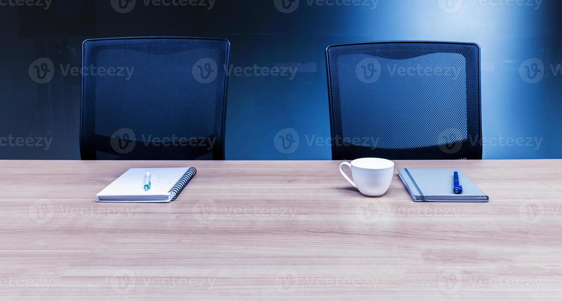 Coffee cup and notebook on table with two black armchairs in meeting room photo