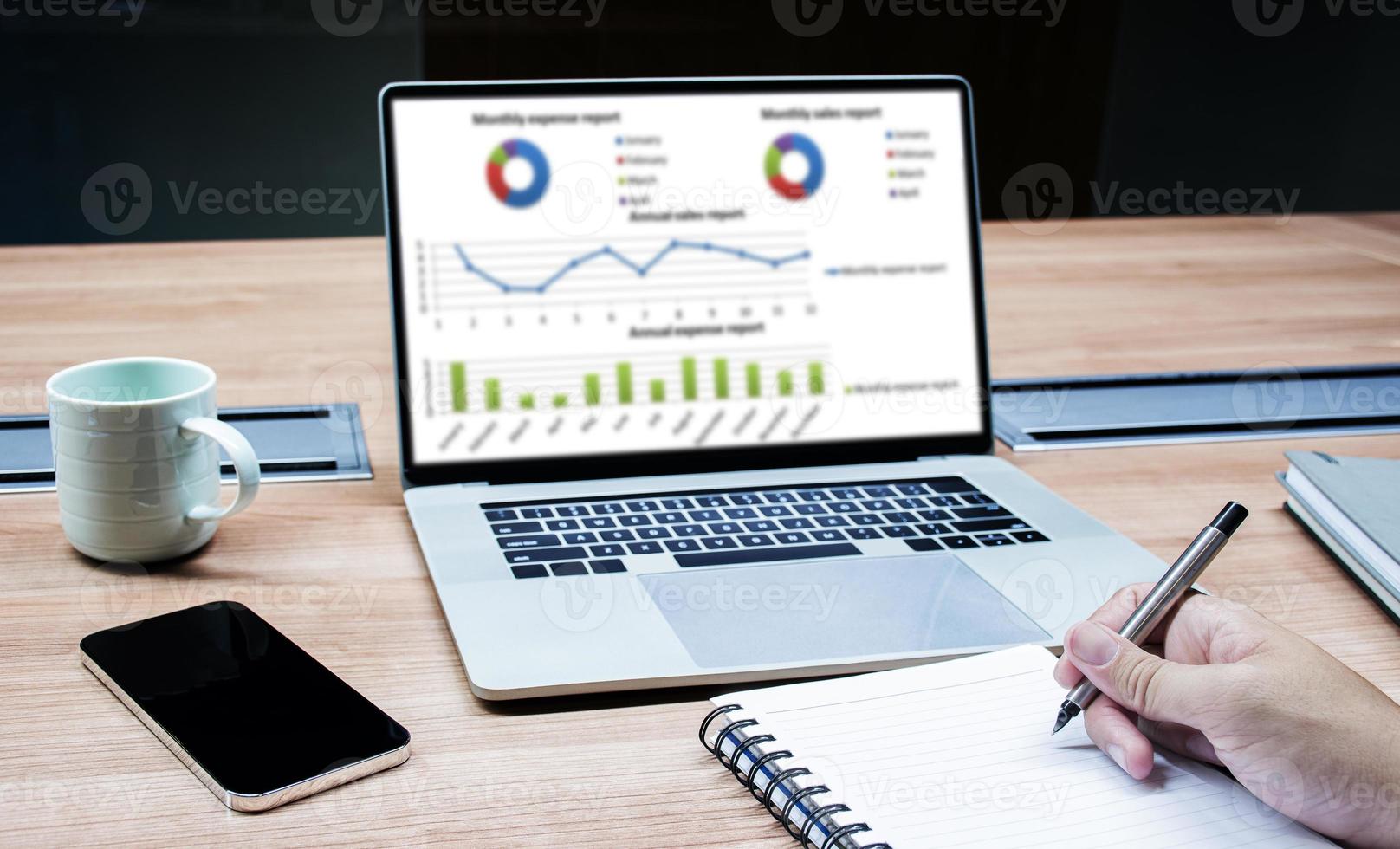 Businessman hand holding a pen to paperwork with laptop on table photo