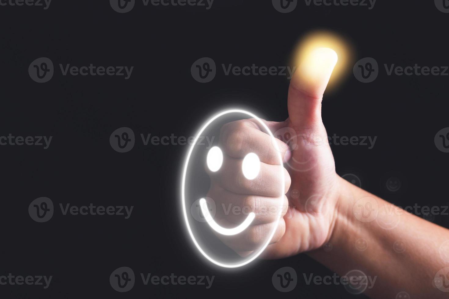 Evaluation and satisfaction concept. Hand shows thumb up sign with smile emoji face. Close up shot on black background. photo