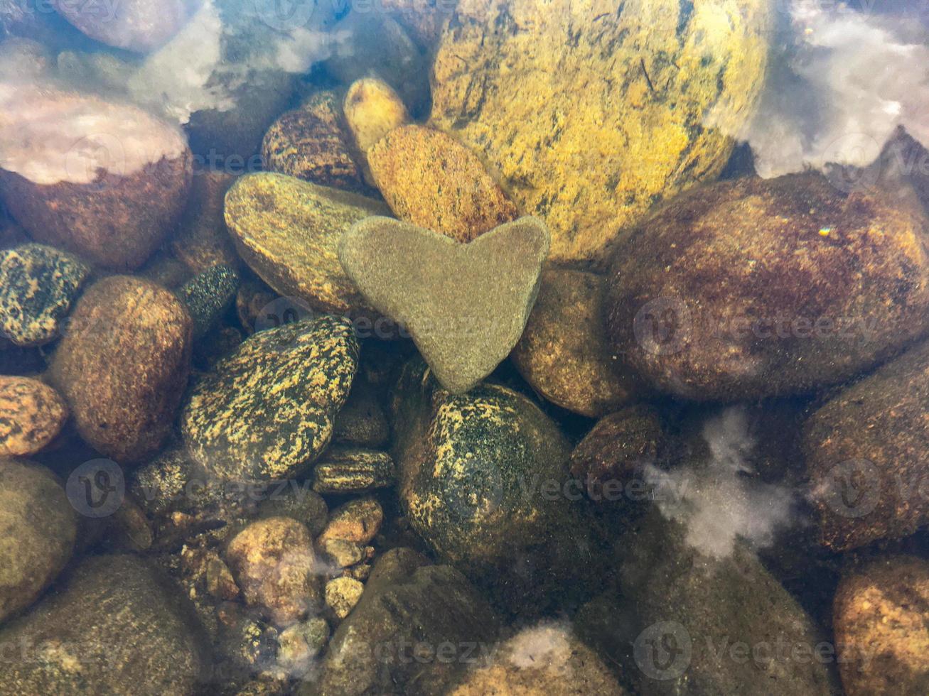 The heart-shaped stone lies at the bottom of the river, horizontal orientation photo