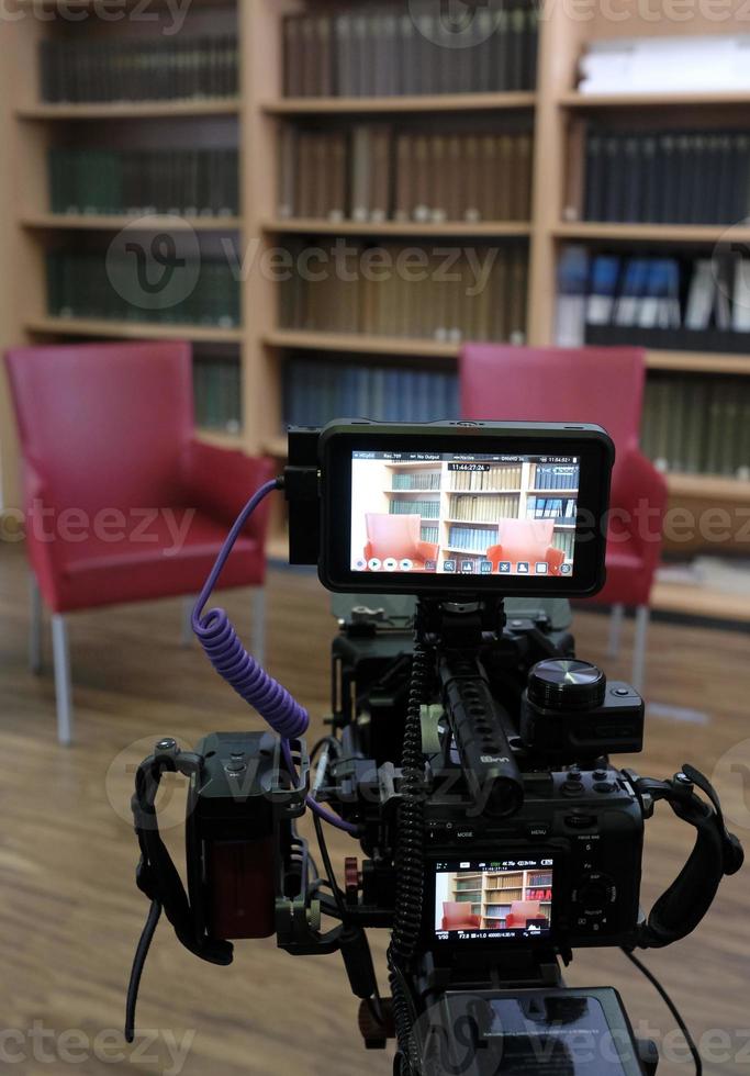 dos sillas vacías en un estudio de televisión con un panel de libros al fondo y una cámara en primer plano foto