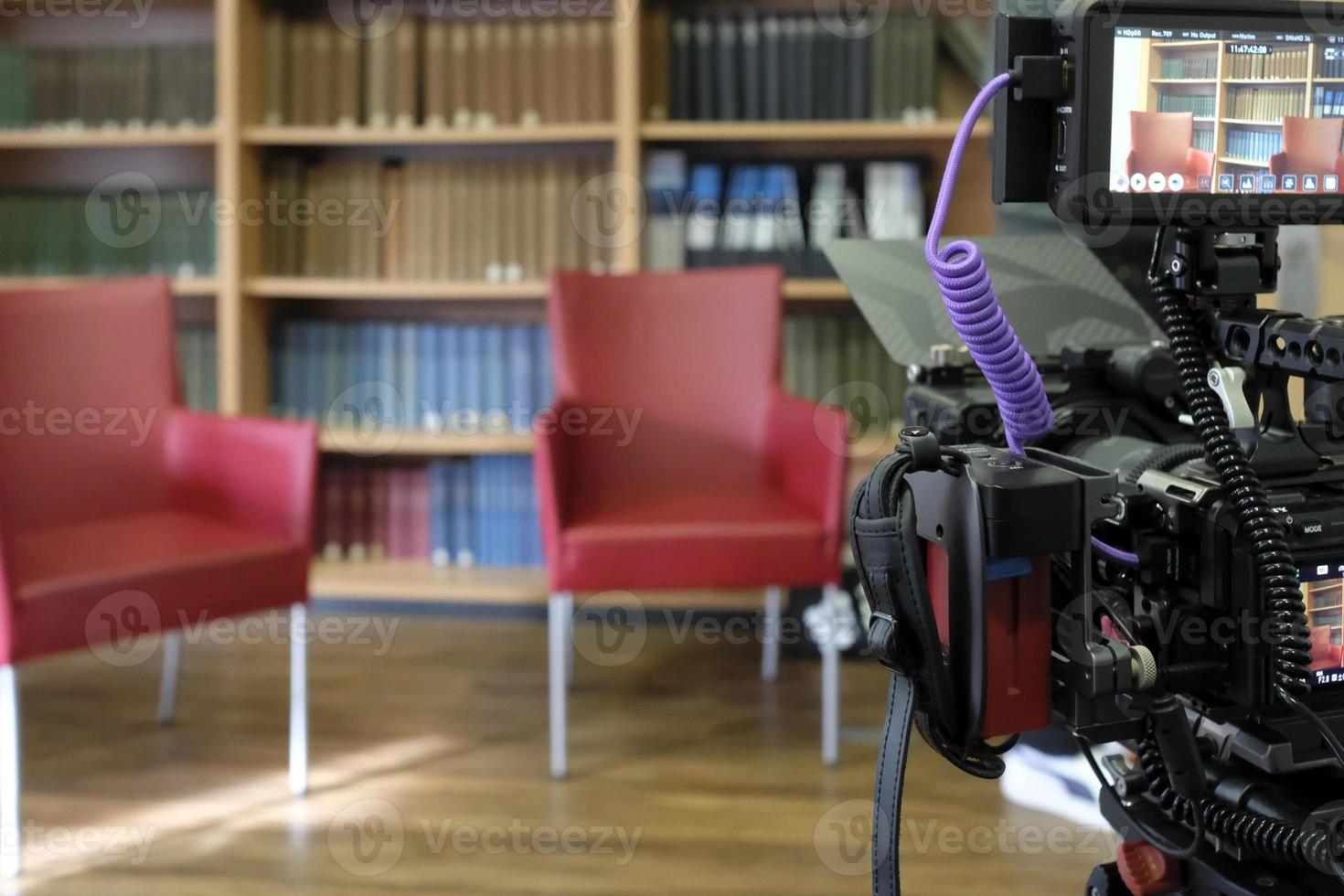 dos sillas vacías en un estudio de televisión con un panel de libros al fondo y una cámara en primer plano foto