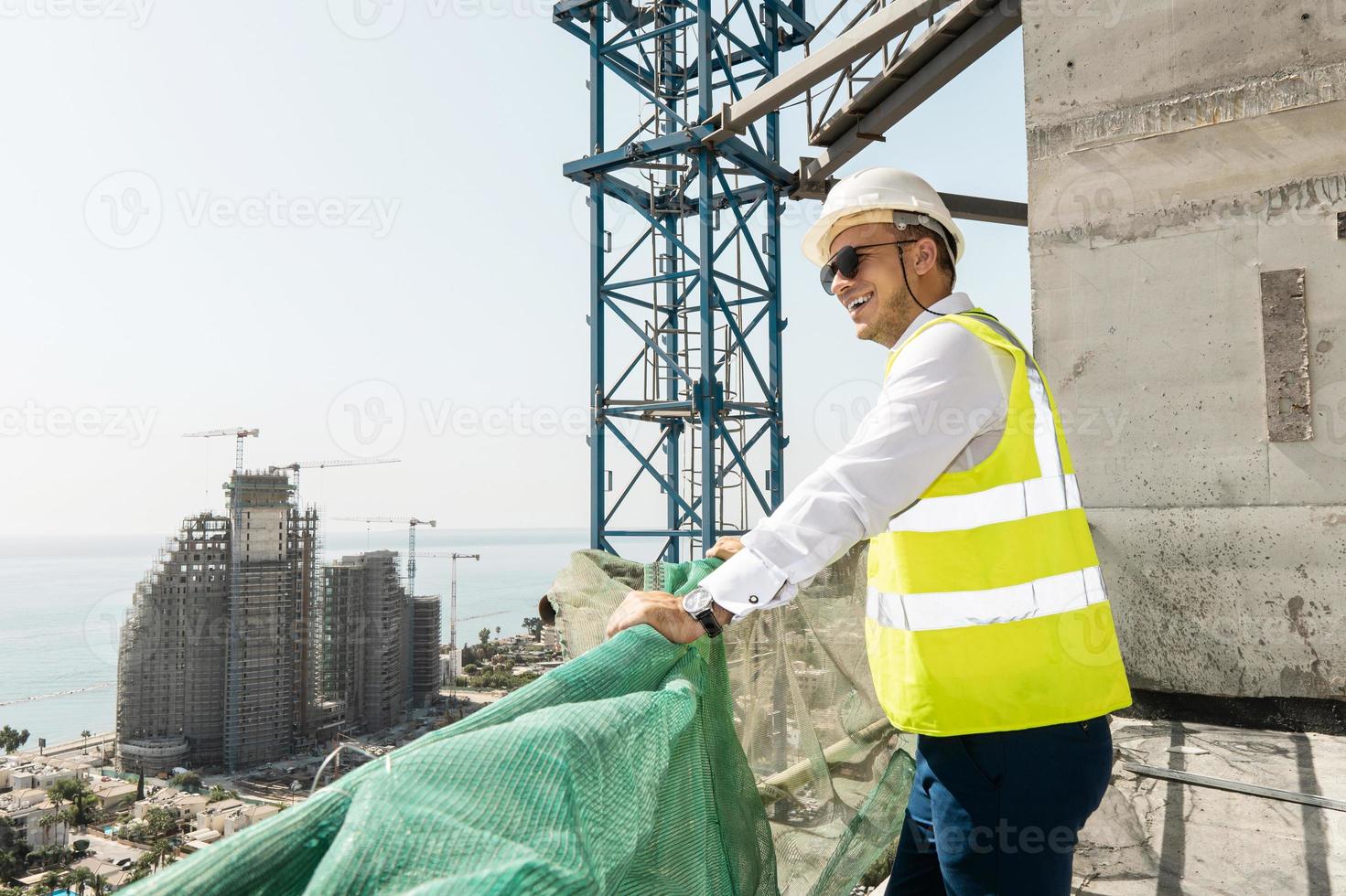 Successful engineer  wearing reflective vest and hard hat on a construction site near blue sea photo