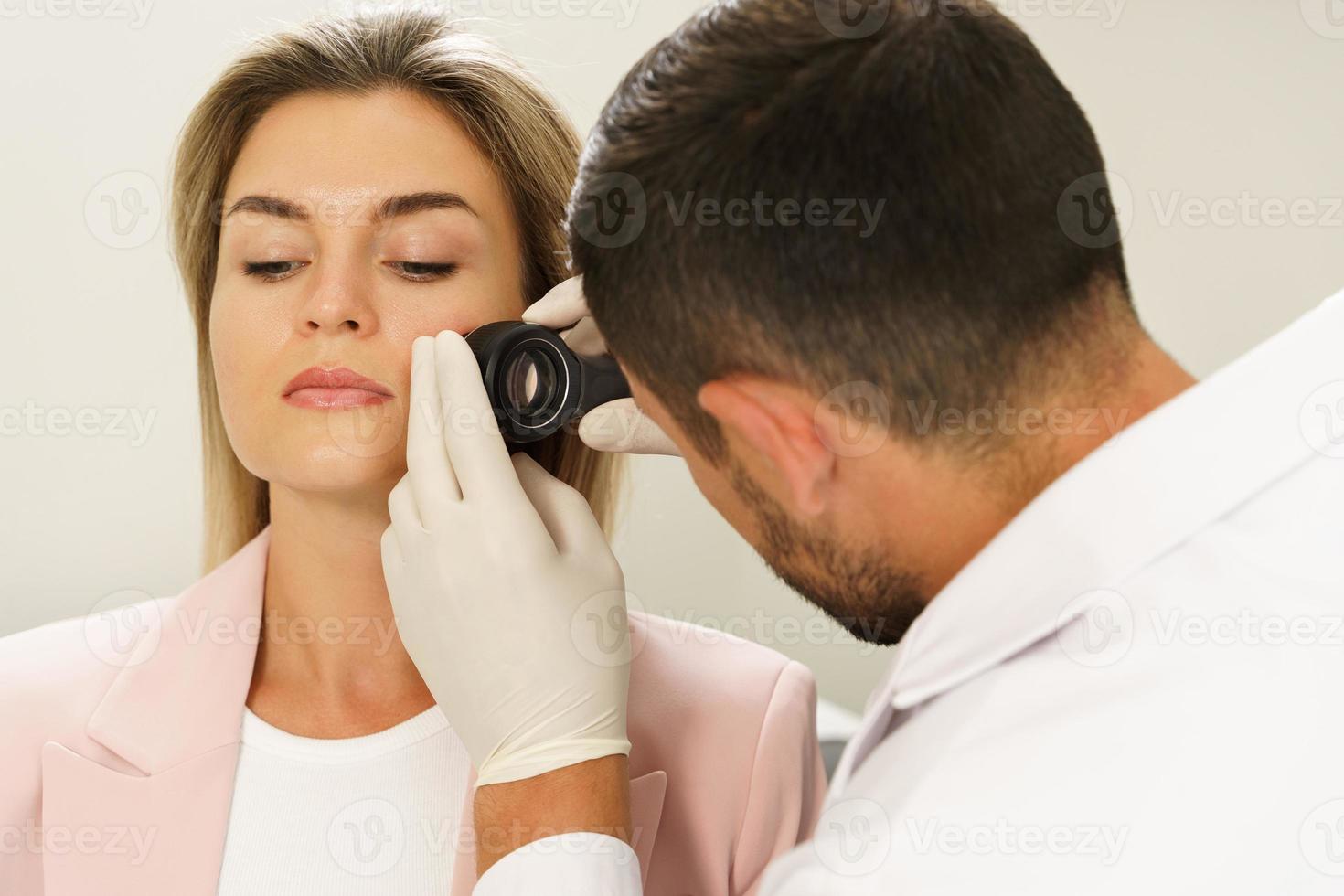 Dermatologist is using dermatoscope for facial skin examination photo