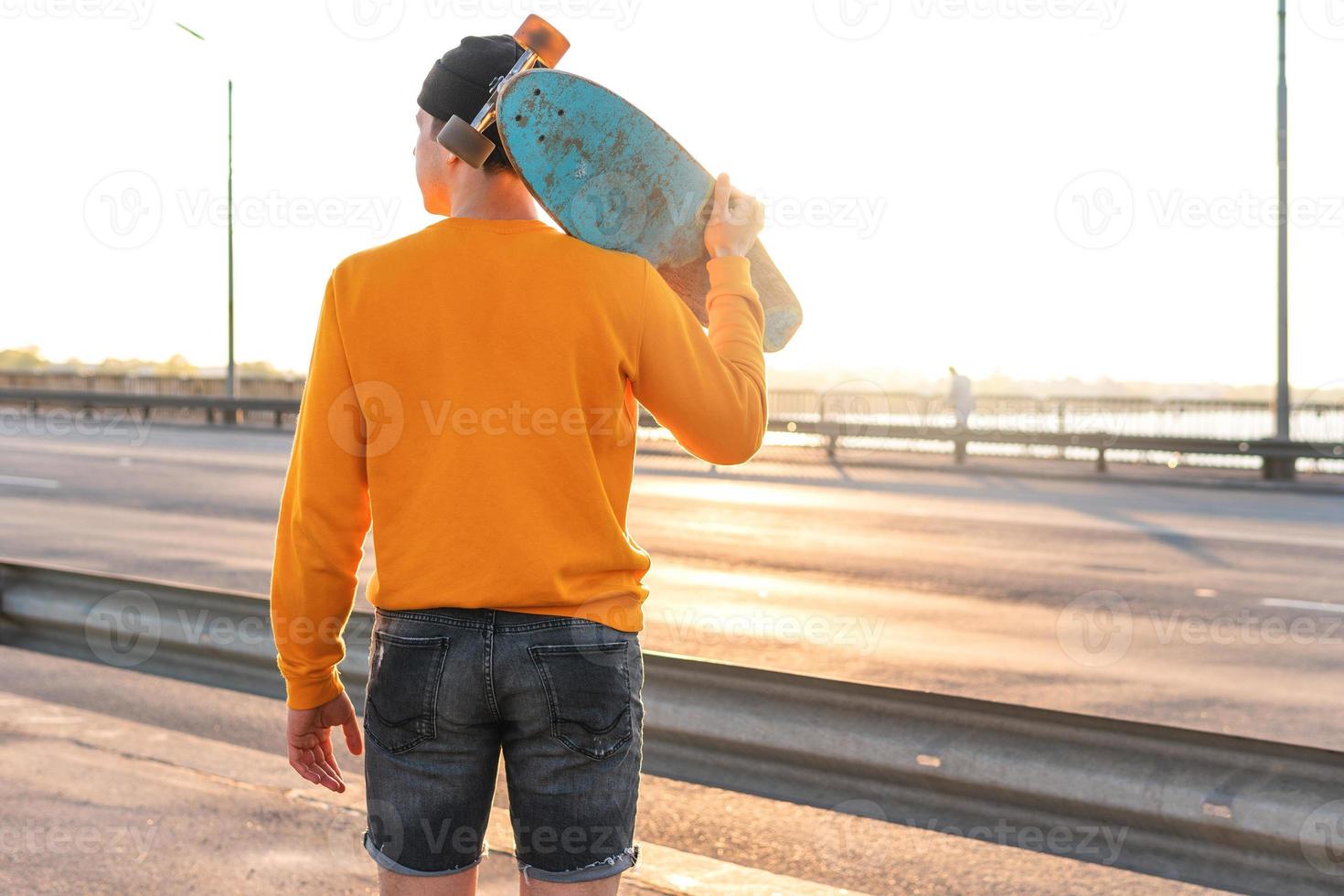 Young man with a longboard on a bridge at sunset photo