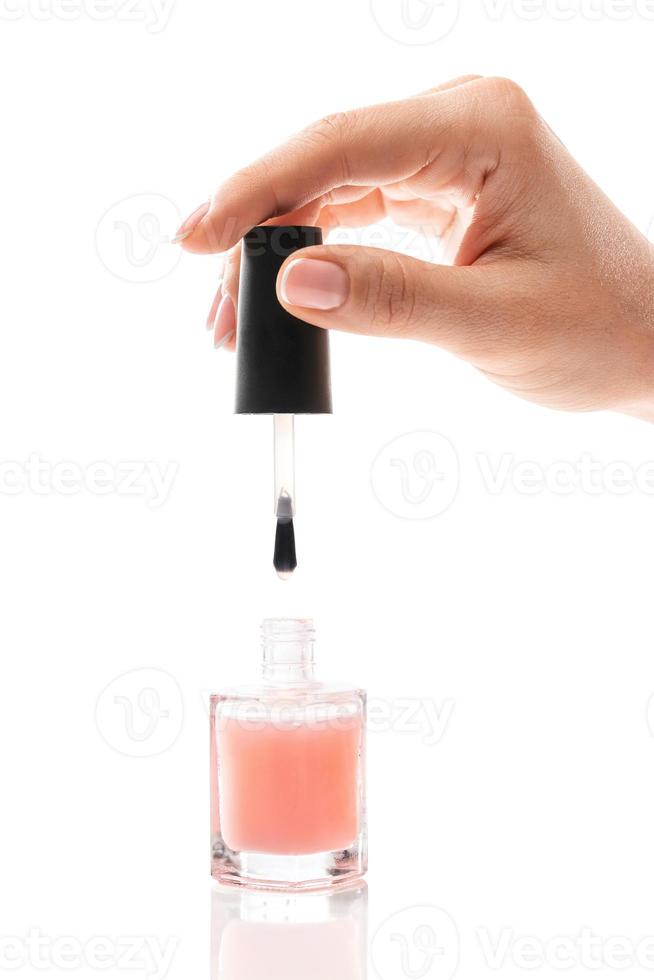 Female hand with beautiful french manicure holding bottle of pink nail polish against white background photo