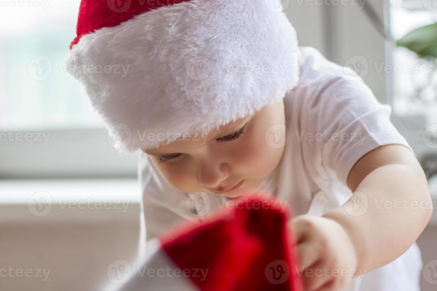 Child boy takes out of the box Christmas toys to dress up the tree. The Christmas tree is lit up and the baby looks at the Christmas toys with pleasure and joyful emotions. photo