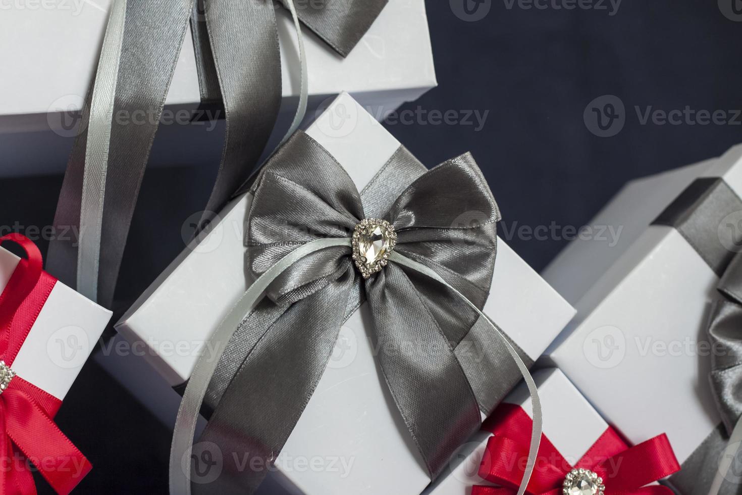 Many gifts. The gift box is white with a red and gray beautiful bow. Gift on a dark background. Holidays and surprises. Satin bows with rhinestones. photo