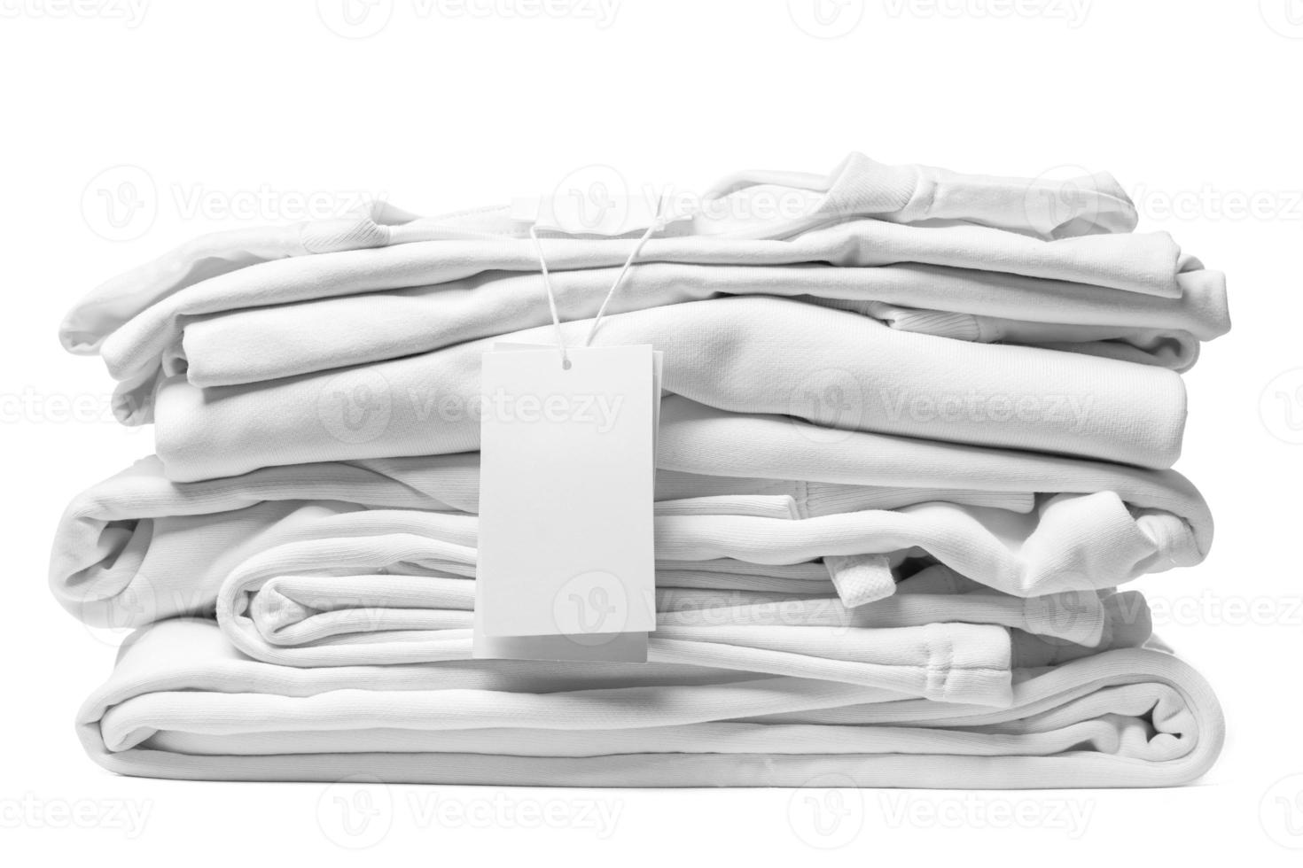 Stack of white clothes with a blank garment tag on white background photo
