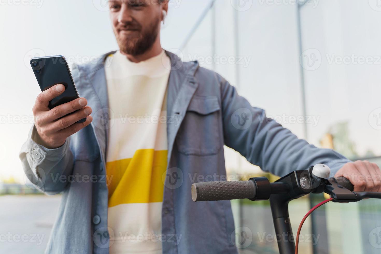 Man with e-scooter using  scooter-sharing system application on his smartphone photo