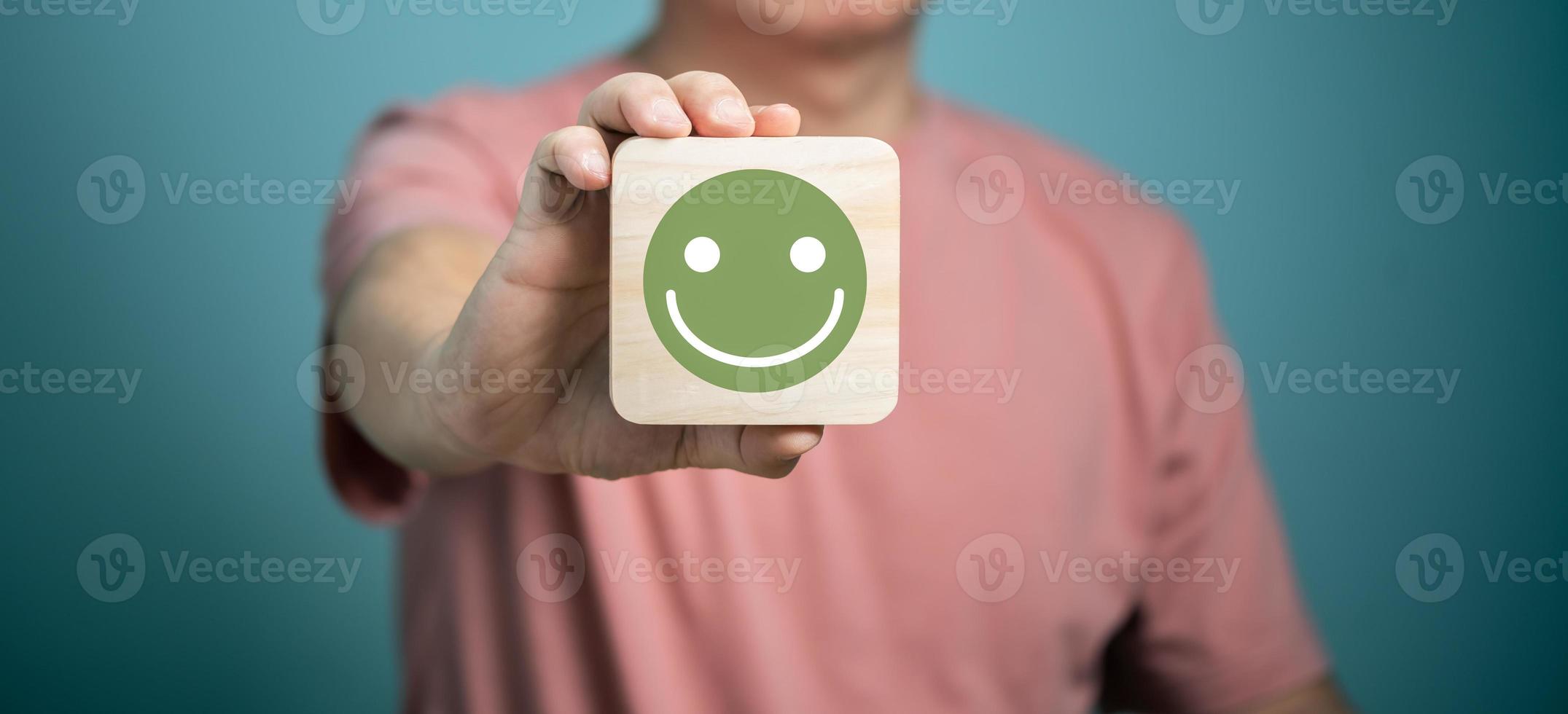 hombre sosteniendo un disco de madera con íconos de cara sonriente, servicio de satisfacción del cliente, comentarios, calificación y revisión del cliente, experiencia, día mundial de la salud mental, pensar en un concepto positivo foto