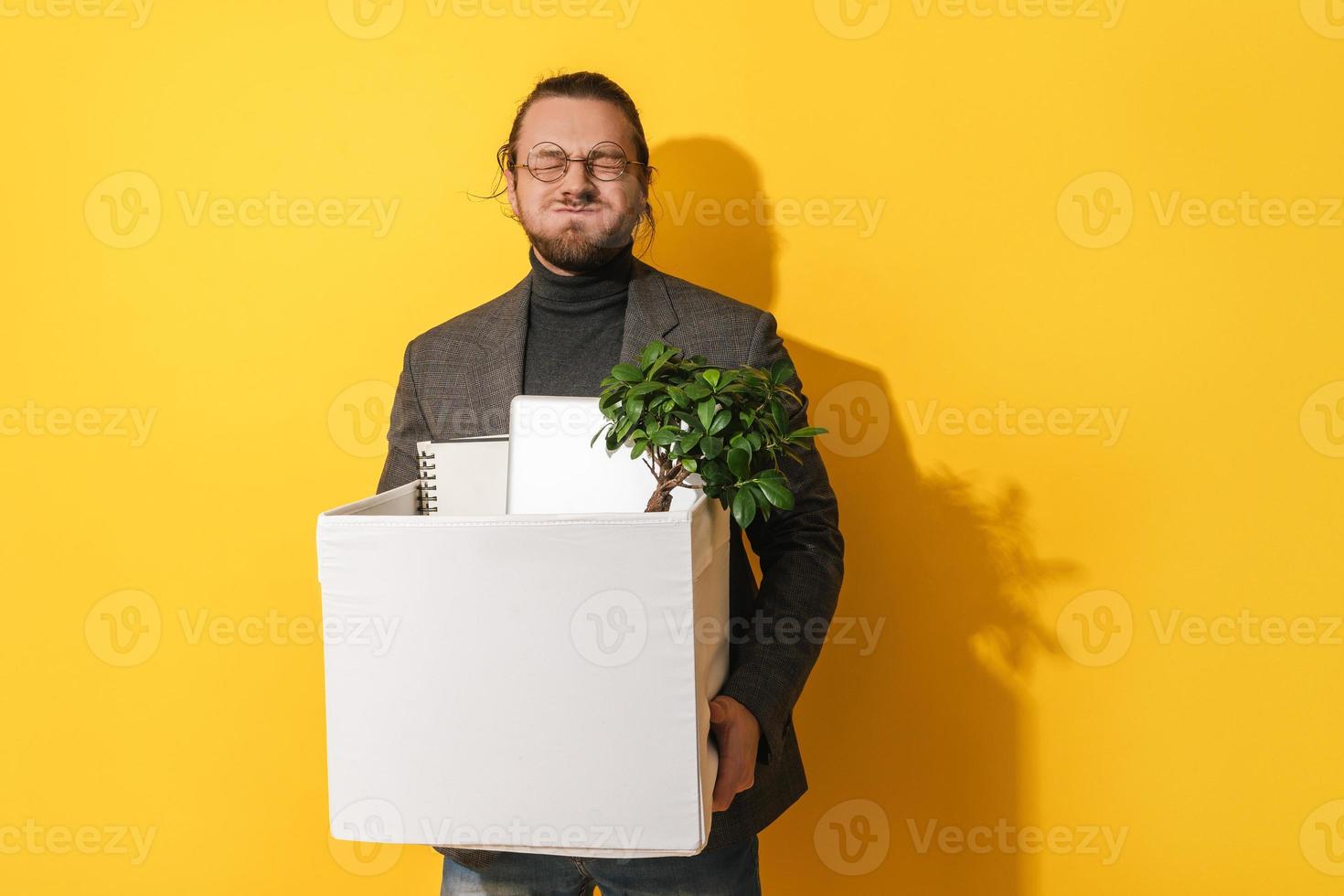 Man with silly face holding box with personal items after resignation against yellow background photo