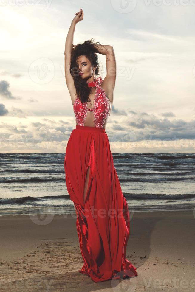 impresionante mujer con un hermoso vestido rojo en la playa foto