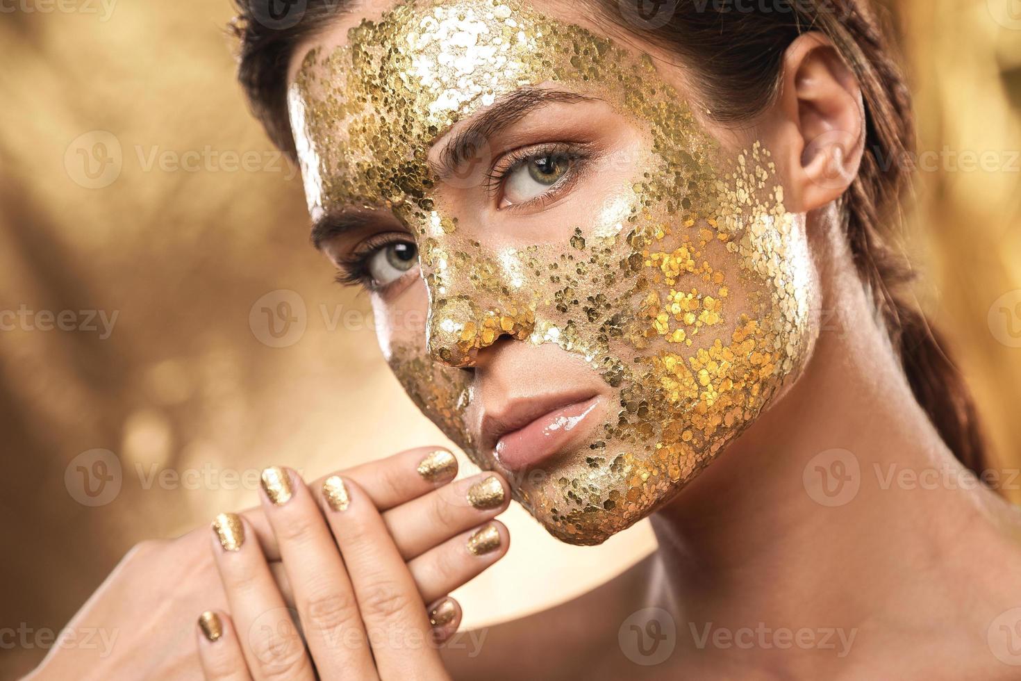 Beautiful woman with golden shining mask on her face for skin treatment photo