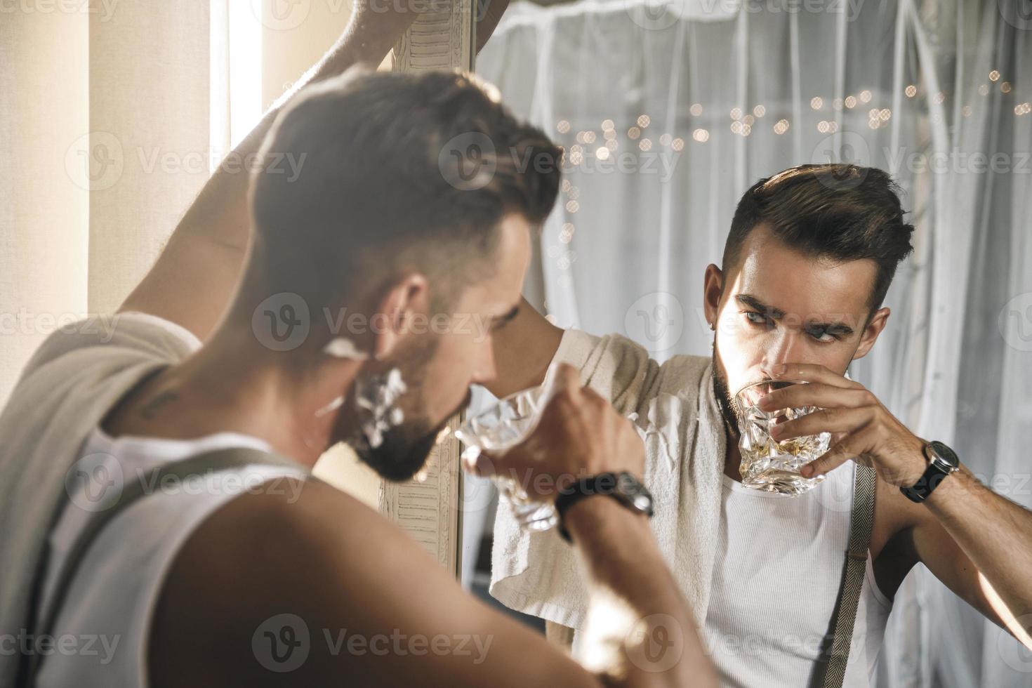 Handsome man with a glass of whiskey is looking in the mirror photo