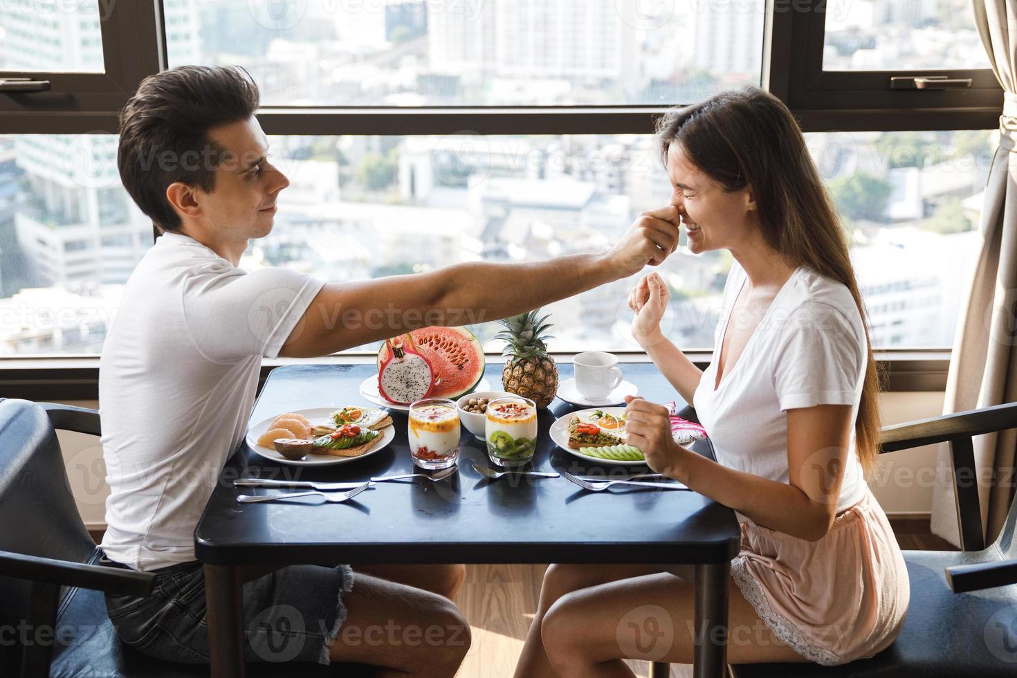 pareja feliz comiendo un desayuno saludable en un apartamento moderno con grandes ventanales y vistas a la ciudad foto