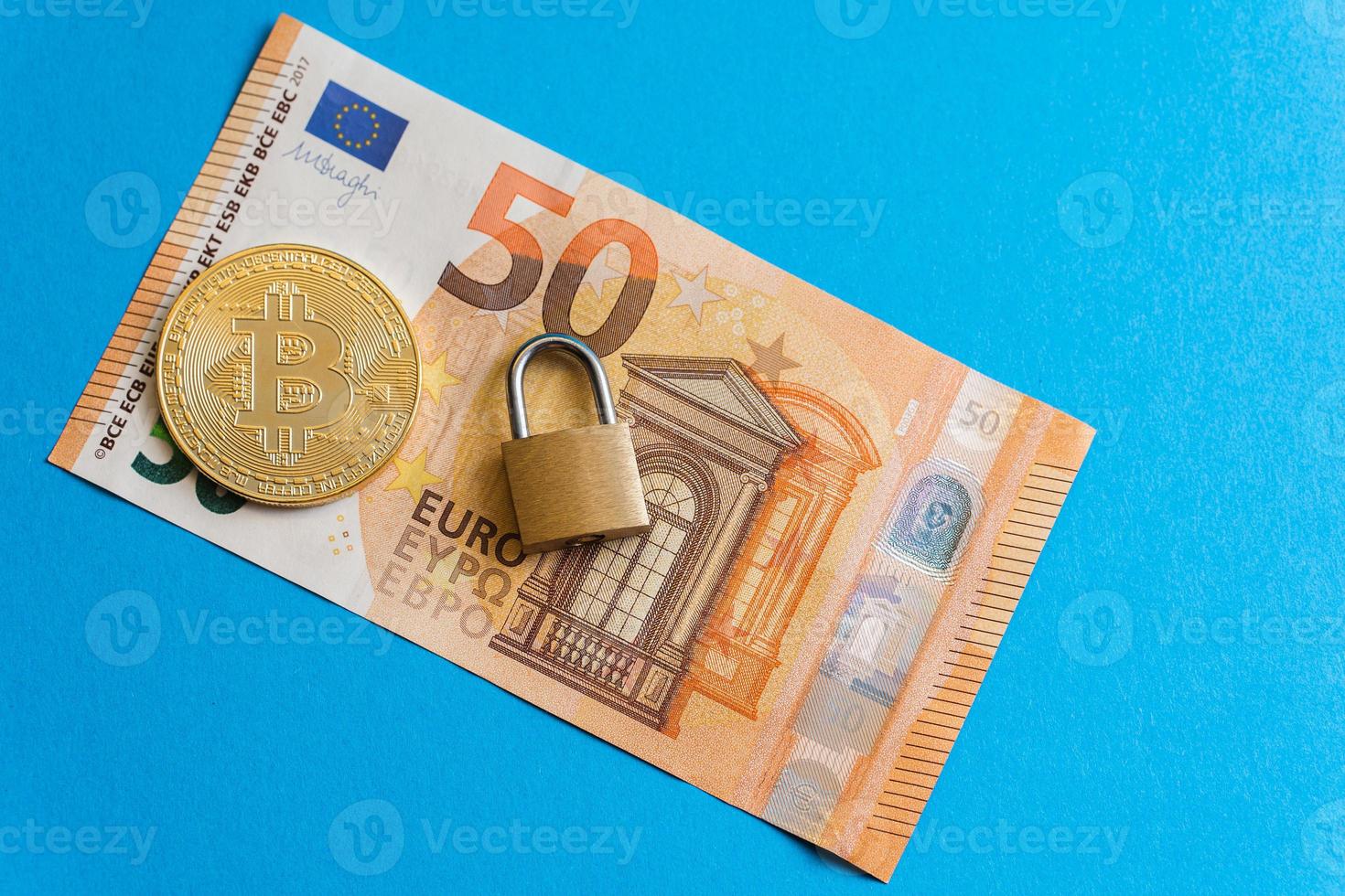 Shiny golden bitcoin and small brass padlock on a fifty euro banknote. photo