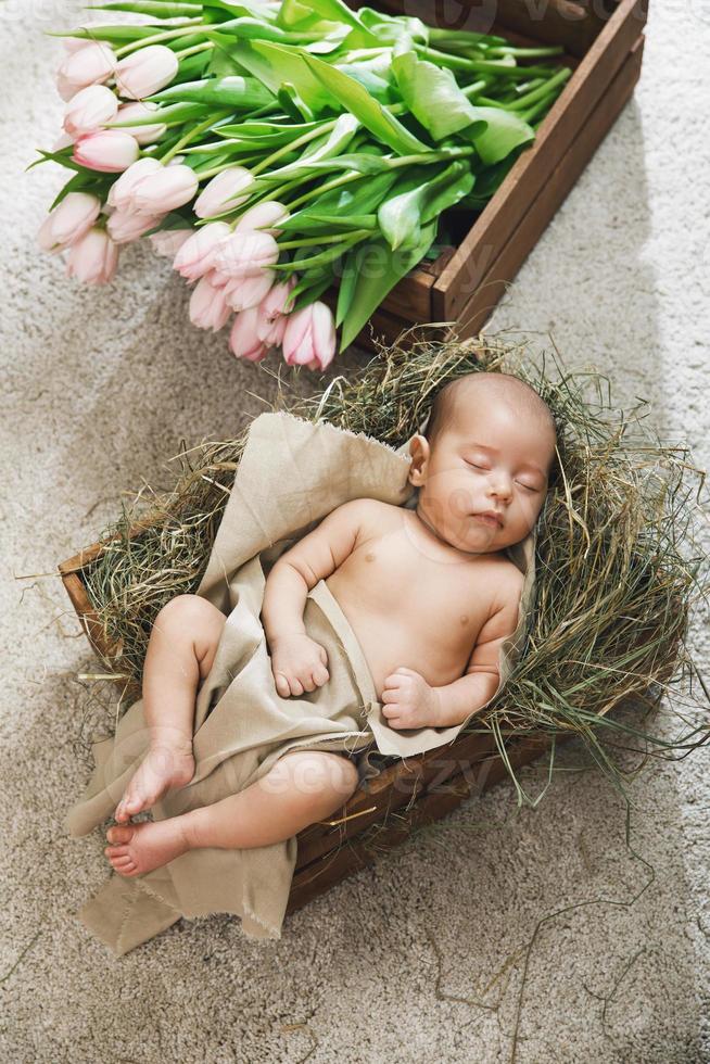 Cute little baby is lying in the wooden box and heap of pink tulips photo
